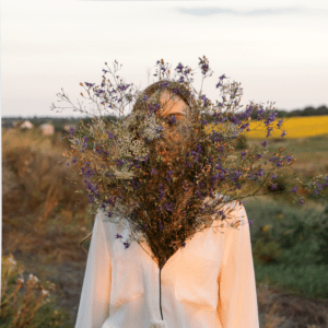 foto de uma mulher com uma planta florescendo de dentro da roupa que ela veste. Ao fundo plantas.